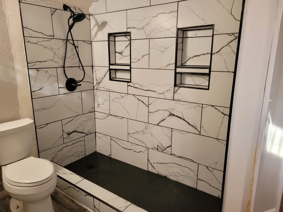 Walk-in shower during the remodel: large white marble-look tile, black niches and a matte black shower head